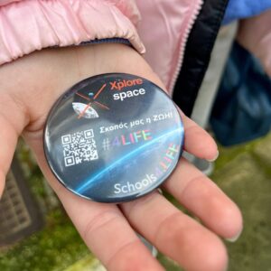 Κοντινό πλάνο μαθητή που κρατά κονκάρδα Xplore Space με μήνυμα «Σκοπός μας η ΖΩΗ» και #4LIFE
